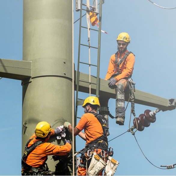 Three technicians performing maintenance work on a power pole