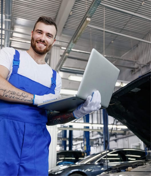 A mechanic holding a laptop performing maintenance on an automobile