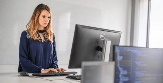 A young woman standing at a desk and typing code into a computer