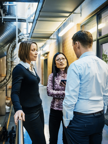 Three standing people are in a discussion